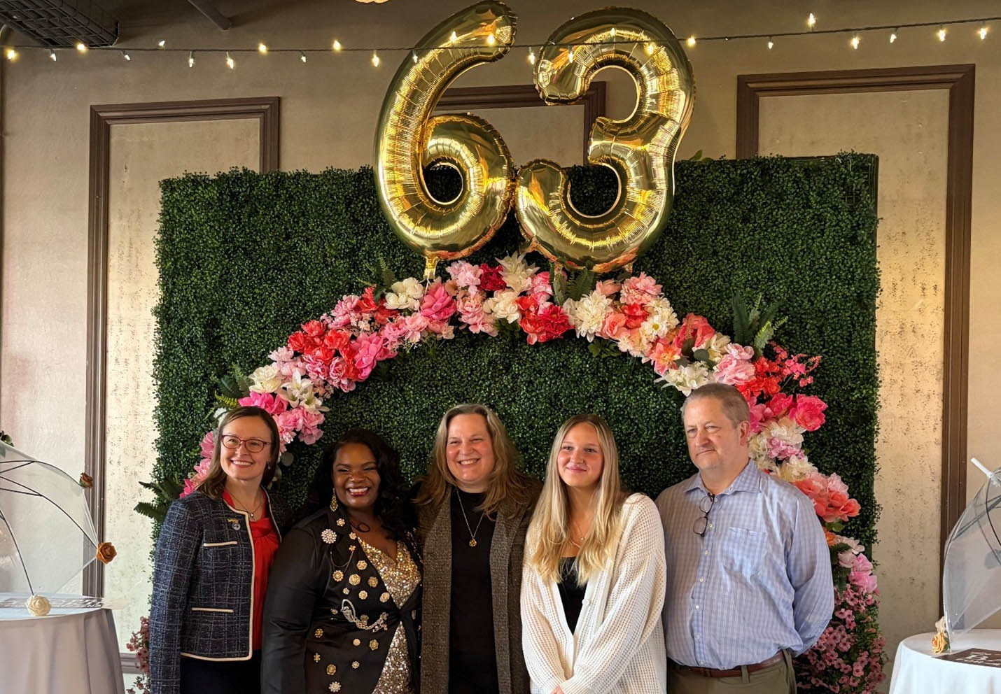 a group of people smiling in front of a green background with a 63 balloon